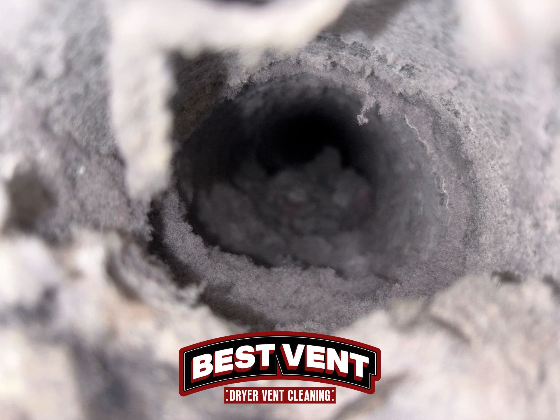 Close-up view inside a dryer vent pipe severely obstructed by thick, grey lint and dust.