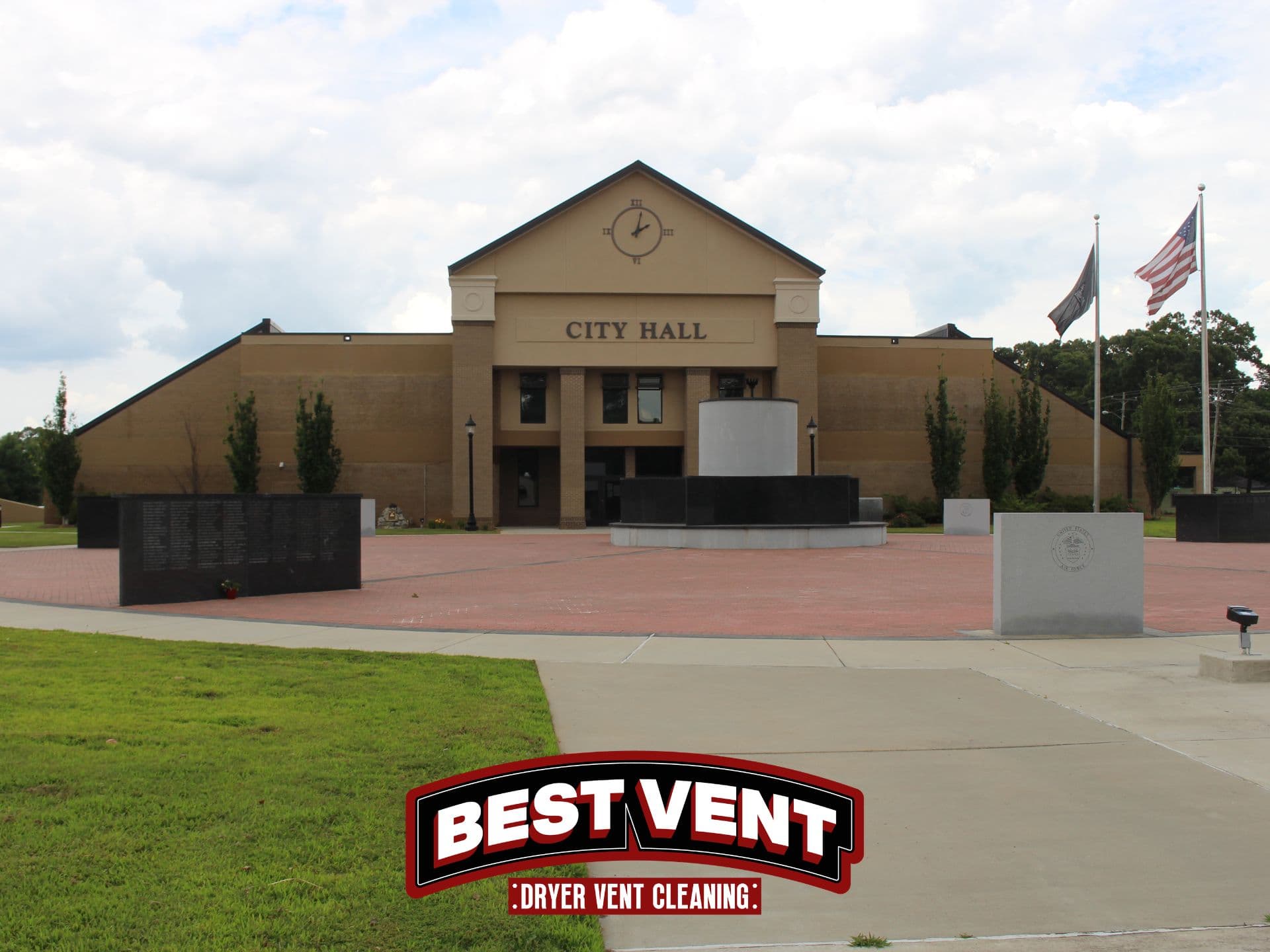 Tan City Hall building with a clock pediment overlooking a brick plaza with stone monuments.