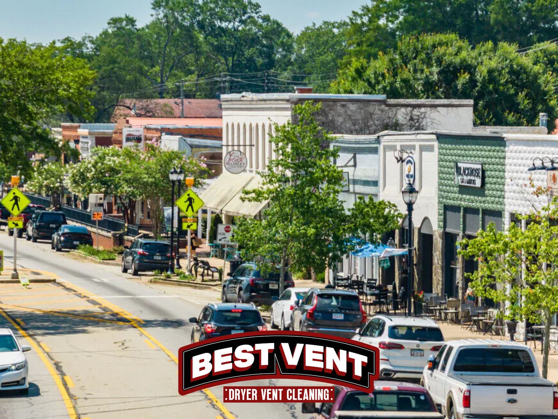 Small-town main street with storefronts and cars, featuring a Best Vent Dryer Vent Cleaning logo.