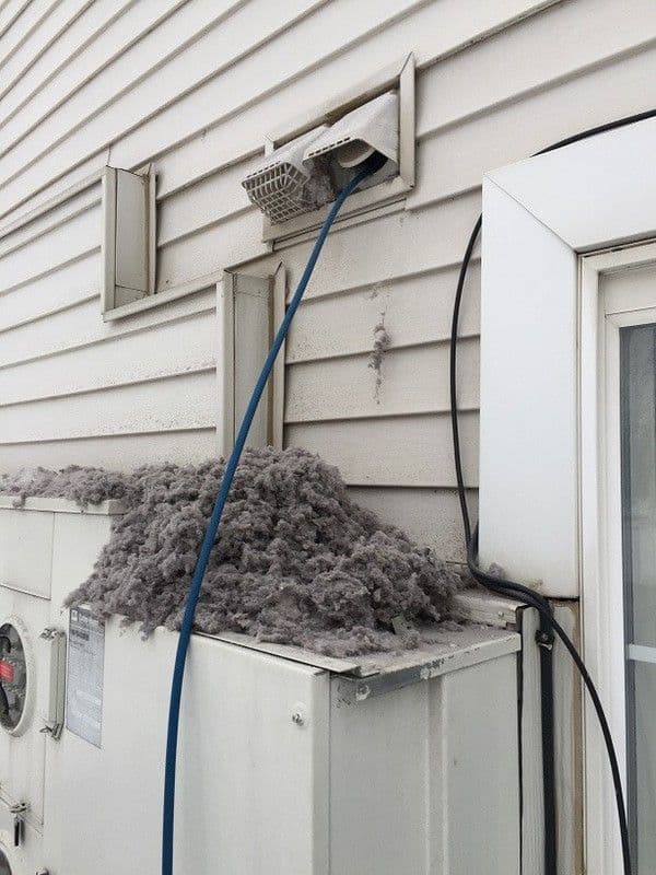 Massive pile of grey dryer lint accumulated on a utility box below an exterior vent.